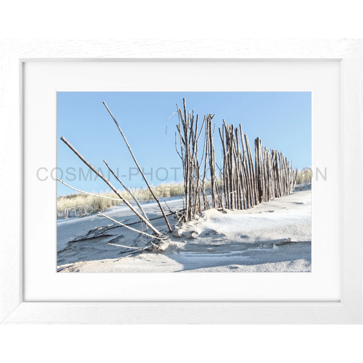 Holzpfeiler und Äste ragen aus schneebedecktem Sand an einem Strand in Sylt