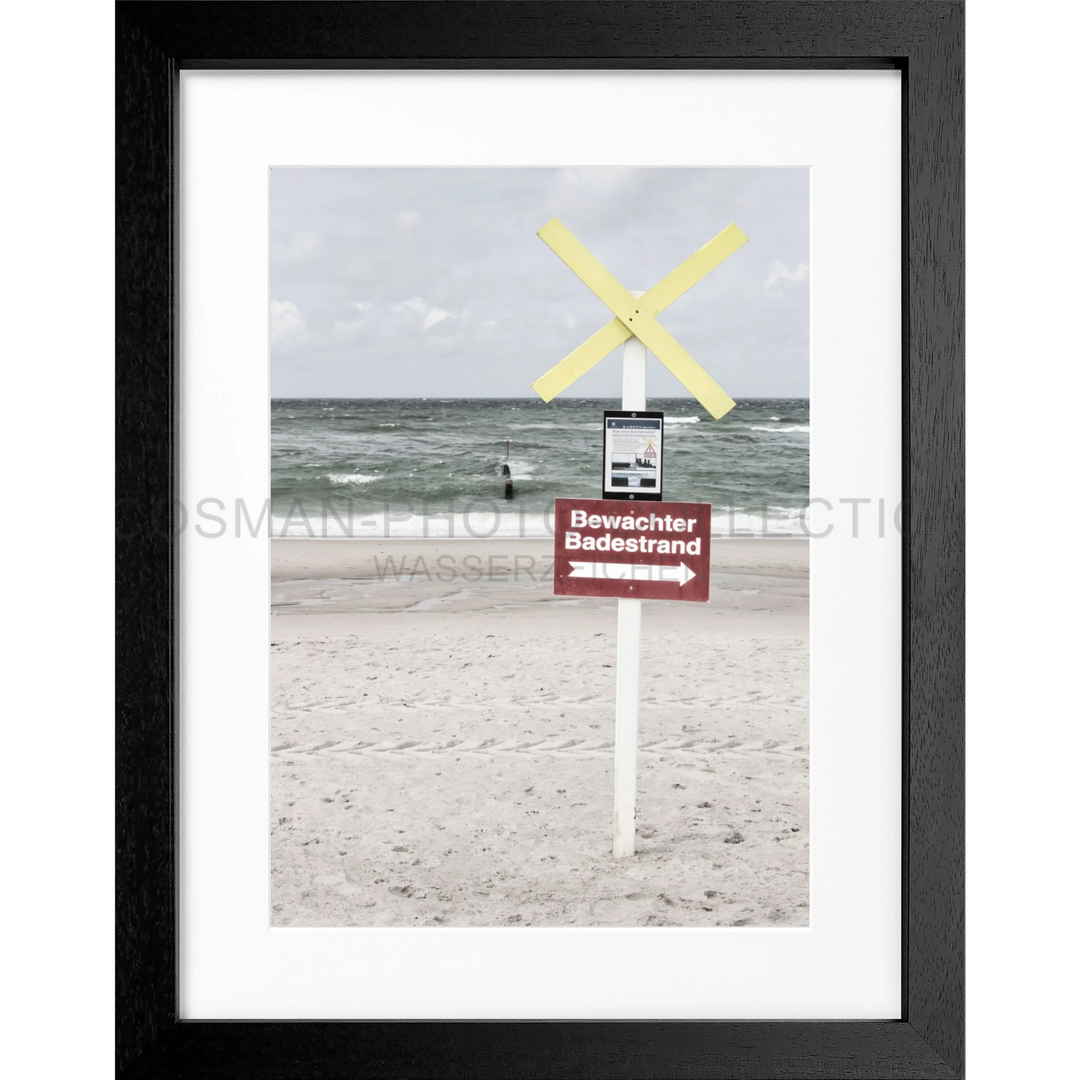 Warnschild mit gelbem Kreuz an einem weißen Pfosten am Strand von Sylt